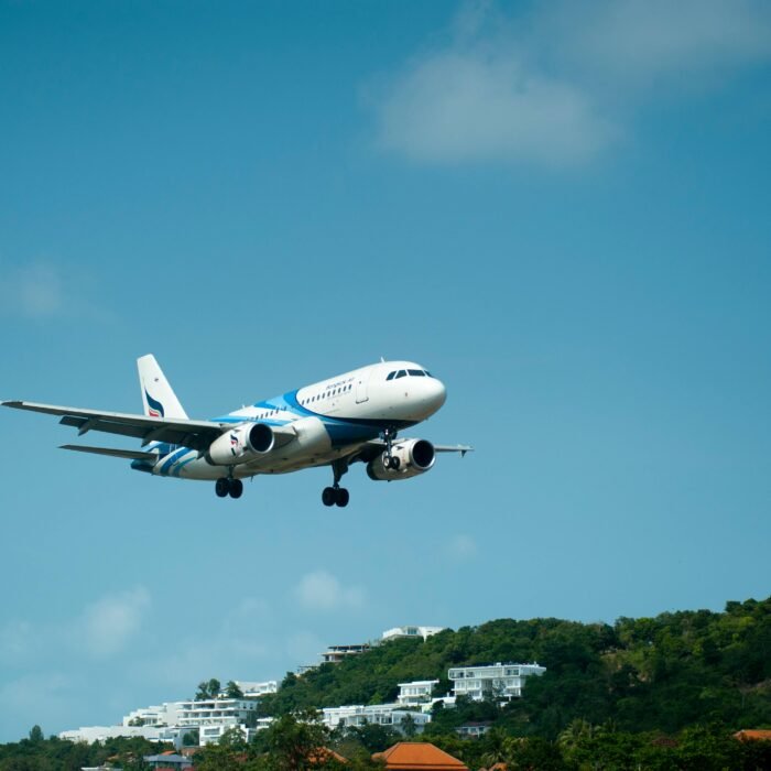 A passenger airplane descends for landing over lush hills in sunny Thailand.